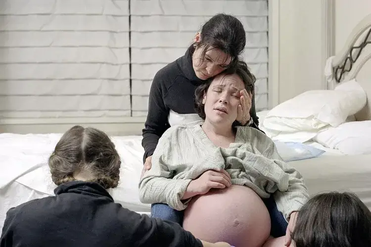 A labouring woman being held by her doula. Her head is being supported by the doula's hand. 