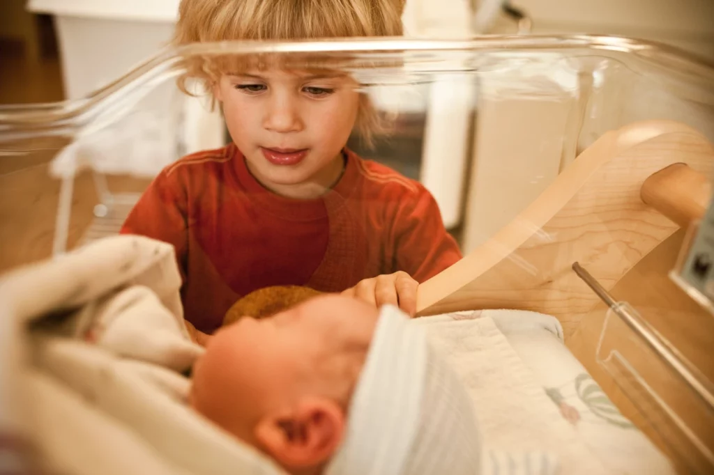 older brother looking and baby sister in crib